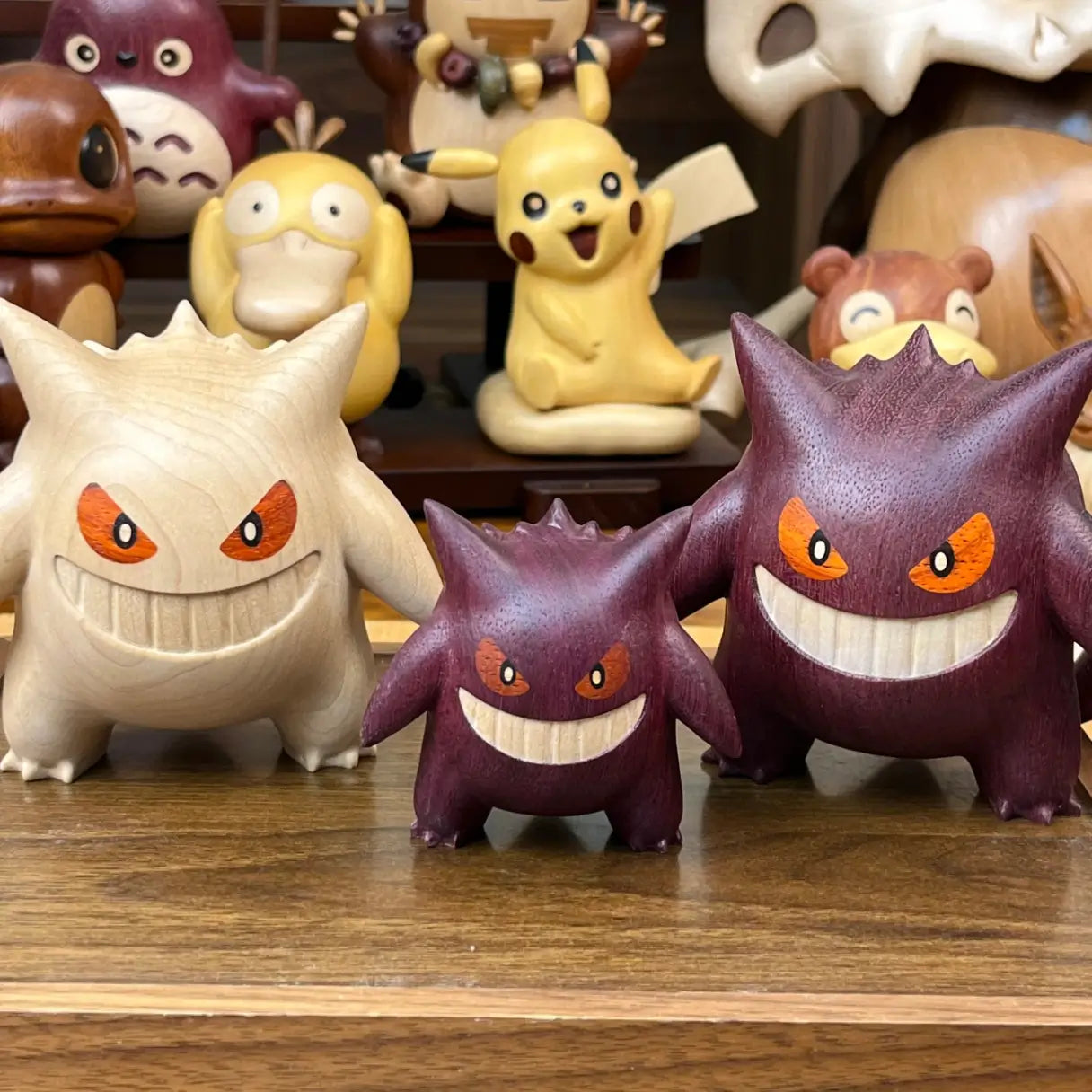 Hand holding a Shiny Gengar wooden figure with other wooden Pokémon figures in the background